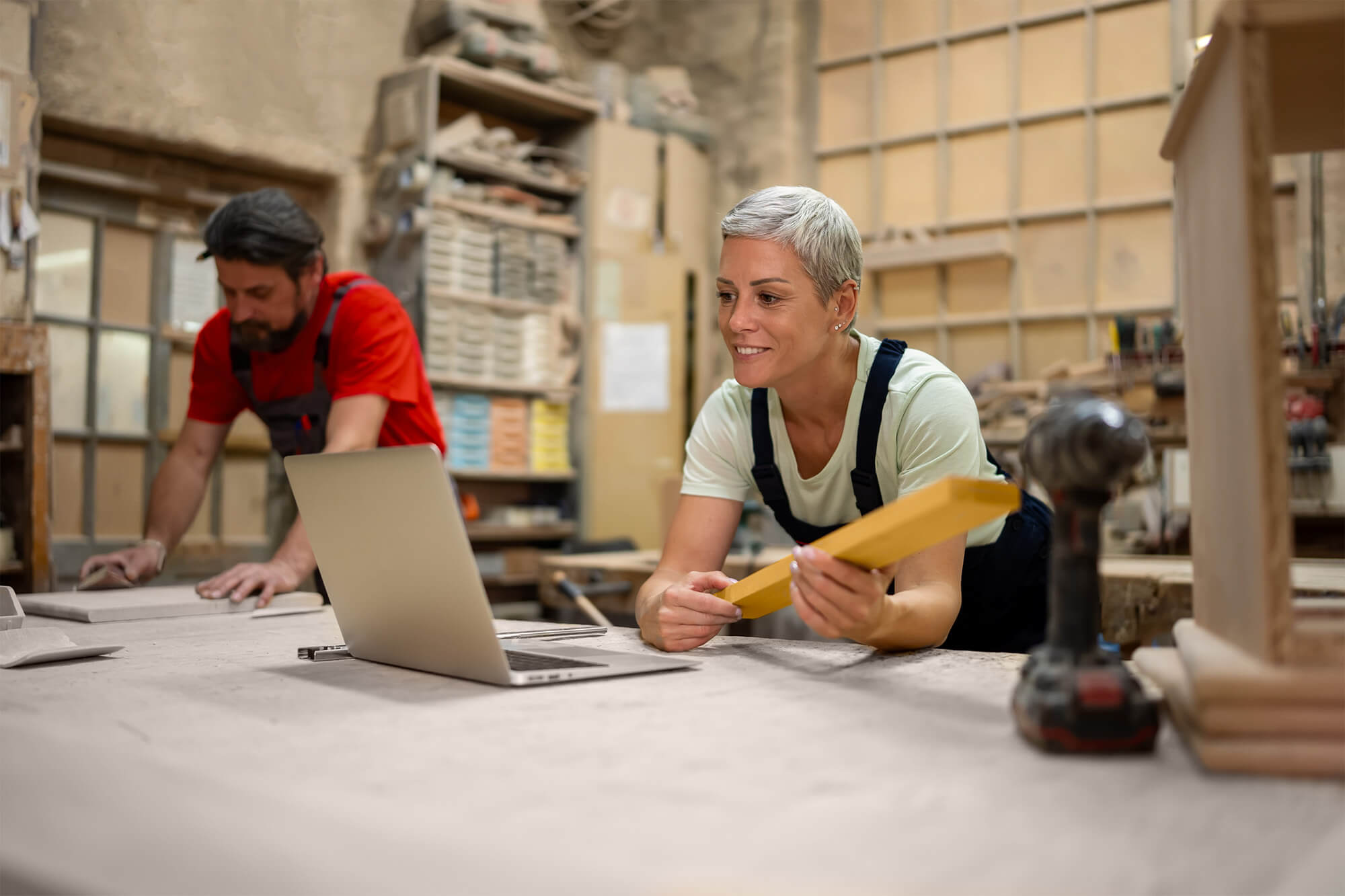 Two people using a laptop in a woodworking workshop.